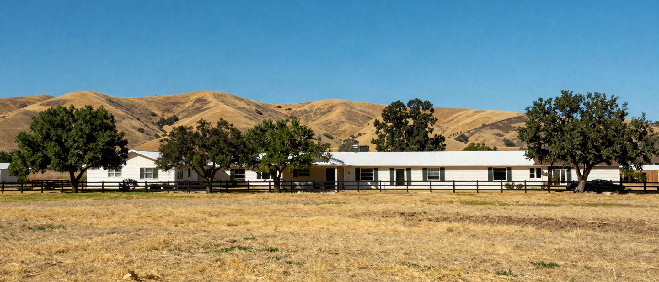 A long low Sonoma County ranch house behind a split rail fence, dry golden hills rising behind it under a deep blue sky.