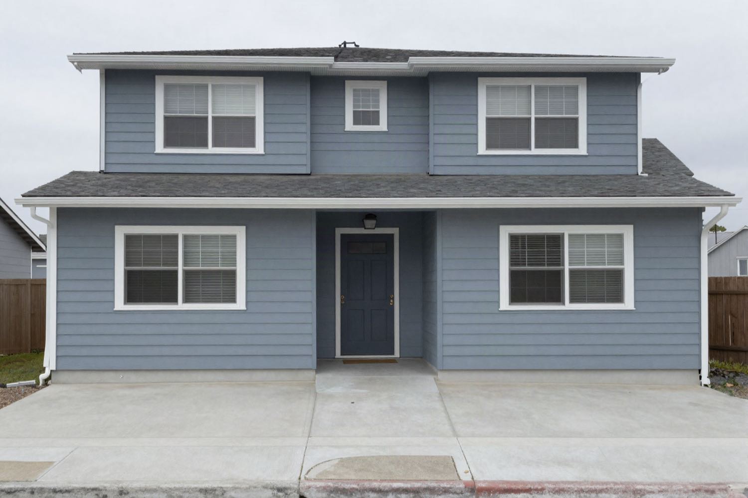 A level straight-on view of the front of a two storey suburban California house in flat overcast light, gutters and downspouts visible.