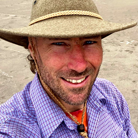 Mark Grumich, smiling, in a felt hat on the Sonoma coast.